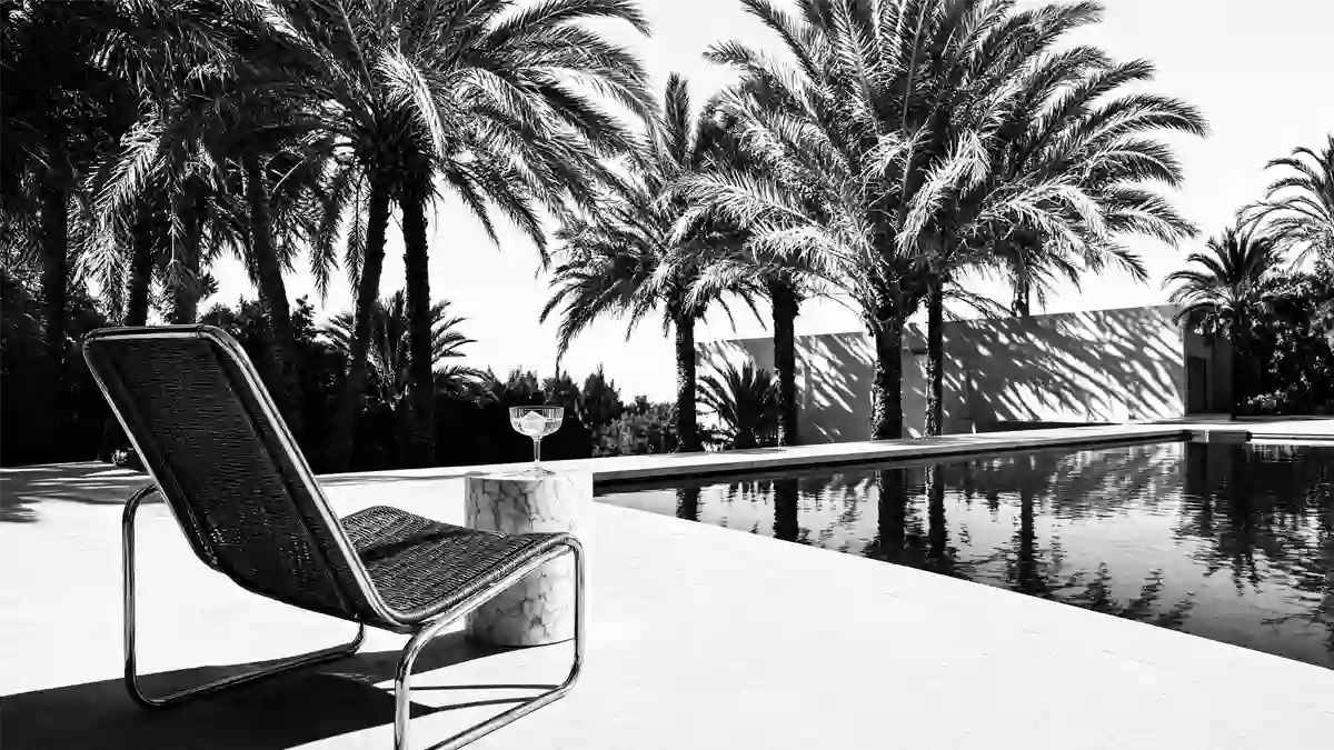 Schwarz-Weiß-Aufnahme einer luxuriösen Poolanlage mit Sonnenliege, Beistelltisch, Cocktailglas und Palmen auf Mallorca.