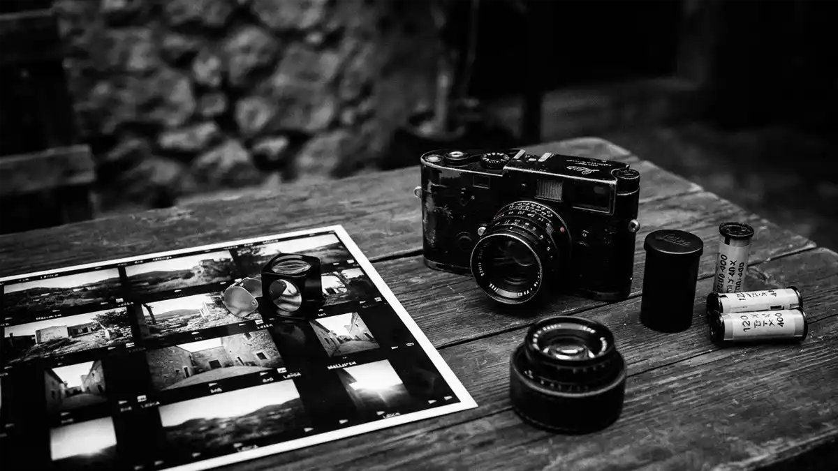 Mallorca PhotoFest 2026: Wenn die ganze Insel zur Fotogalerie wird Analoge Fotografie-Ausrüstung mit Leica-Kamera, Filmrollen und Kontaktabzug auf einem Holztisch für das Mallorca Photofest 2026.
